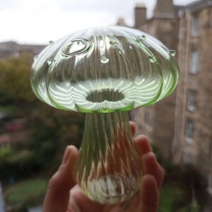May include: A green glass mushroom with a textured surface and small air bubbles. The mushroom is about 6 inches tall.