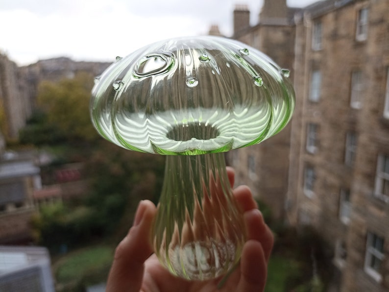 May include: A green glass mushroom with a textured surface and small air bubbles. The mushroom is about 6 inches tall.