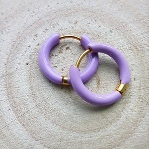 May include: A pair of lavender hoop earrings with a gold accent. The earrings are made of a thick, rounded material.