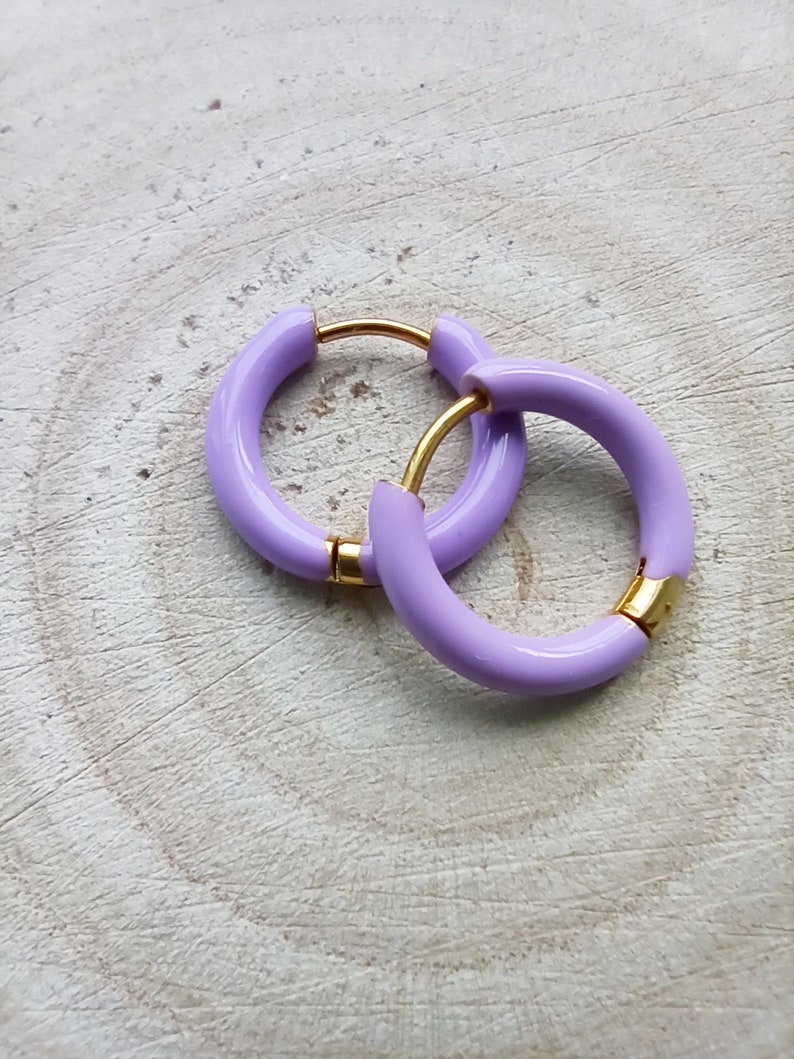 May include: A pair of lavender hoop earrings with a gold accent. The earrings are made of a thick, rounded material.