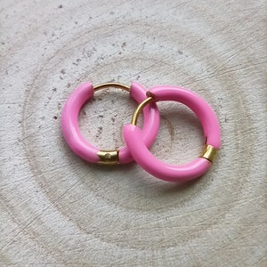 May include: A pair of pink hoop earrings with a gold accent. The earrings are made of a smooth, glossy material.