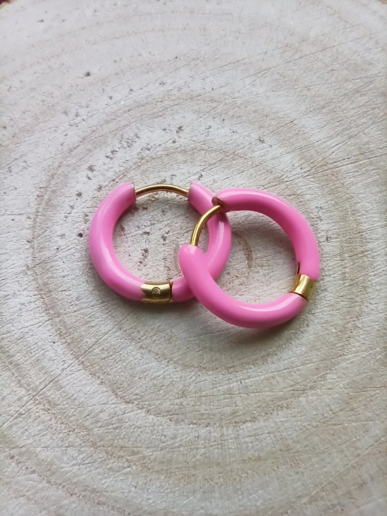May include: A pair of pink hoop earrings with a gold accent. The earrings are made of a smooth, glossy material.