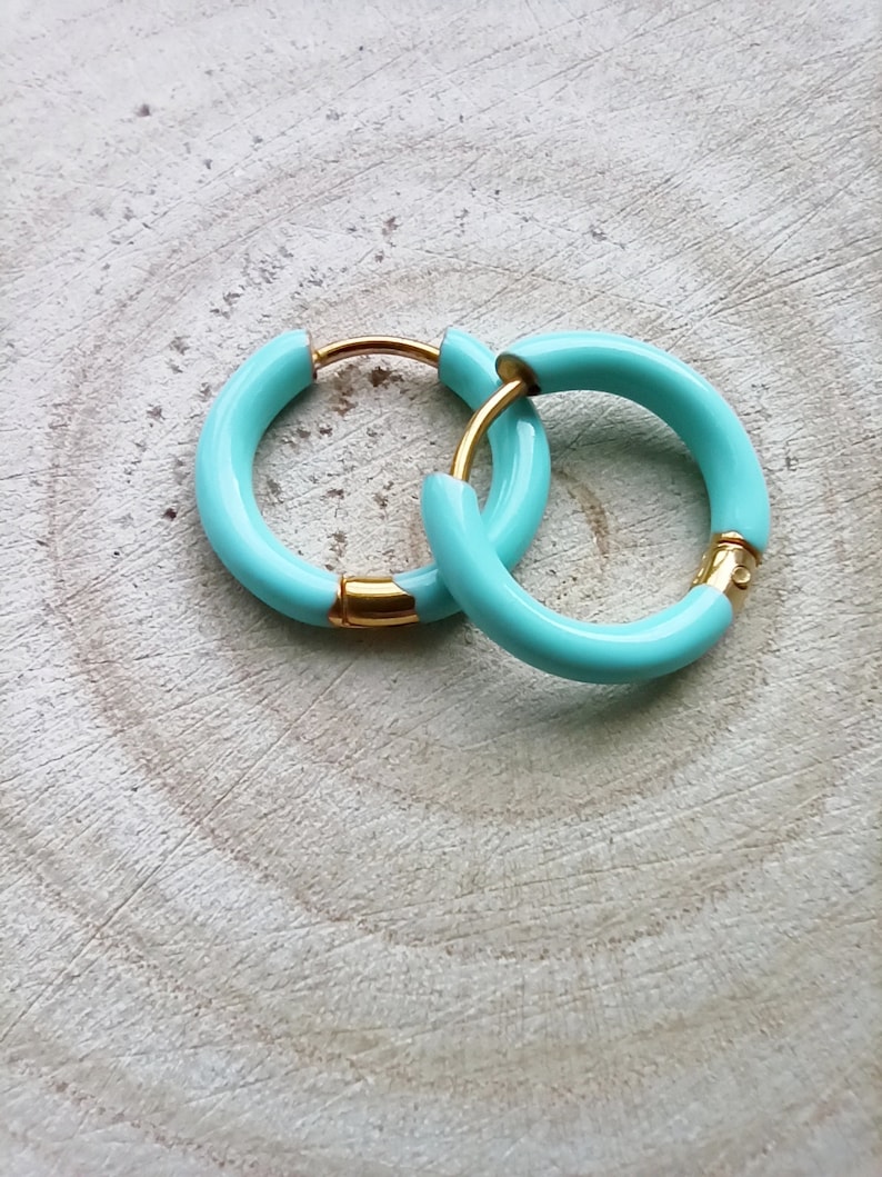 May include: A pair of turquoise hoop earrings with a gold finish. The earrings are simple and elegant.