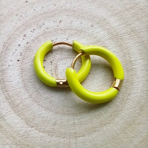 May include: A pair of yellow hoop earrings with a gold metal clasp. The earrings are on a light wood background.