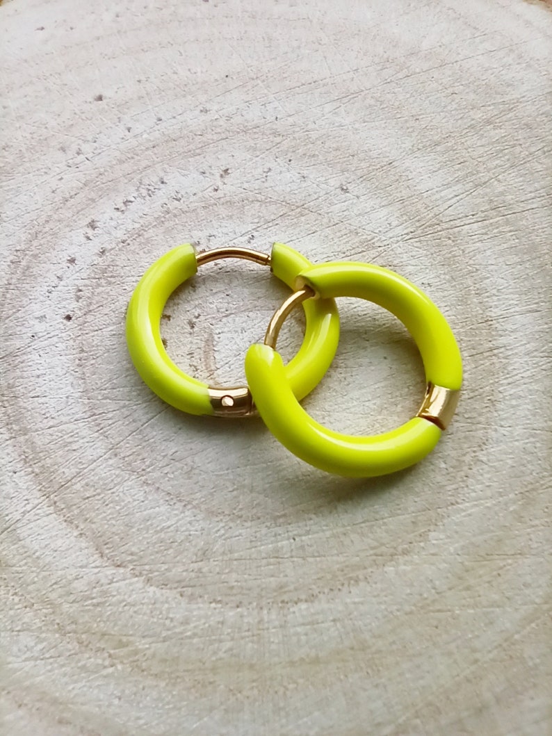 May include: A pair of yellow hoop earrings with a gold metal clasp. The earrings are on a light wood background.