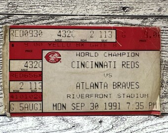 May include: A vintage Cincinnati Reds vs. Atlanta Braves ticket from September 30, 1991, at Riverfront Stadium. The ticket is red and white, with the Cincinnati Reds logo and game details.