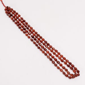 May include: Four strands of faceted, teardrop-shaped, deep red garnet beads. The beads are strung together, creating a necklace-like arrangement. The beads have a polished, reflective surface, and are arranged against a white background.