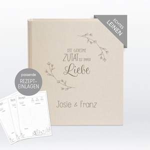 Könnte beinhalten: Ein beiges Rezeptbuch in Leinenbindung mit dem Text "DIE GEHEIME ZUTAT IST IMMER Liebe" und "Josie & Franz" auf dem Einband. Das Buch enthält passende Rezepteinlagen und ein Ecketikett mit der Aufschrift "ECHTES LEINEN".