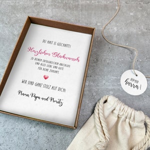 May include: A white card with a pink heart and the text "Du hast es geschafft! Herzlichen Gl&uuml;ckwunsch zu deinem erfolgreichen Abschluss und alles Liebe und Gute f&uuml;r deine Zukunft. Wir sind ganz stolz auf dich! Mama, Papa und Moritz" and a white tag with the text "Hip-Hip hurra!"