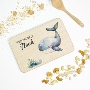 Puede incluir: Una tabla de cortar de madera clara con una ilustración de ballena y el texto "HIER KRUMELT Noah".