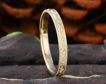 May include: A gold-colored ring with an intricate floral pattern engraved around the band. The ring has a polished finish and a smooth interior. The ring is a classic piece of jewelry.