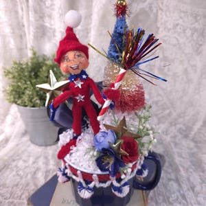 May include: A white ceramic mug with a black handle and the text "But First, Coffee" in a black, handwritten-style font. The mug is on a white surface.