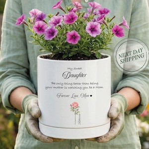 May include: A white ceramic flower pot with a saucer, filled with soil and vibrant pink petunias. The pot has text that reads "My Sweet Daughter" and a message from "Mom". A pink rose illustration is also featured.