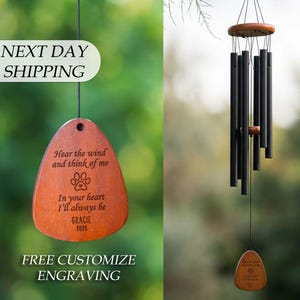 May include: A wind chime featuring black metal tubes suspended from a round wooden top. A wooden pendant hangs at the bottom, engraved with a paw print and the text: Hear the wind and think of me, In your heart I'll always be, GRACIE, 2025.