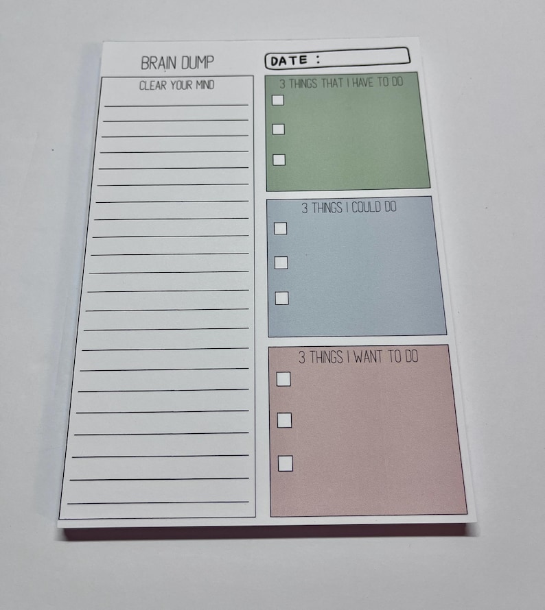 May include: A rectangular notepad with a white background featuring the text BRAIN DUMP and DATE. The left side has lined space labeled CLEAR YOUR MIND. The right side has three colored boxes labeled 3 THINGS THAT I HAVE TO DO, 3 THINGS I COULD DO, and 3 THINGS I WANT TO DO, each with three checkboxes.