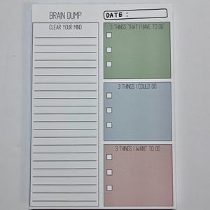 May include: A rectangular paper notepad with a white background featuring a Brain Dump section with horizontal lines. The right side includes three colored boxes labeled 3 Things That I Have To Do in green, 3 Things I Could Do in blue, and 3 Things I Want To Do in pink, each with three checkboxes.