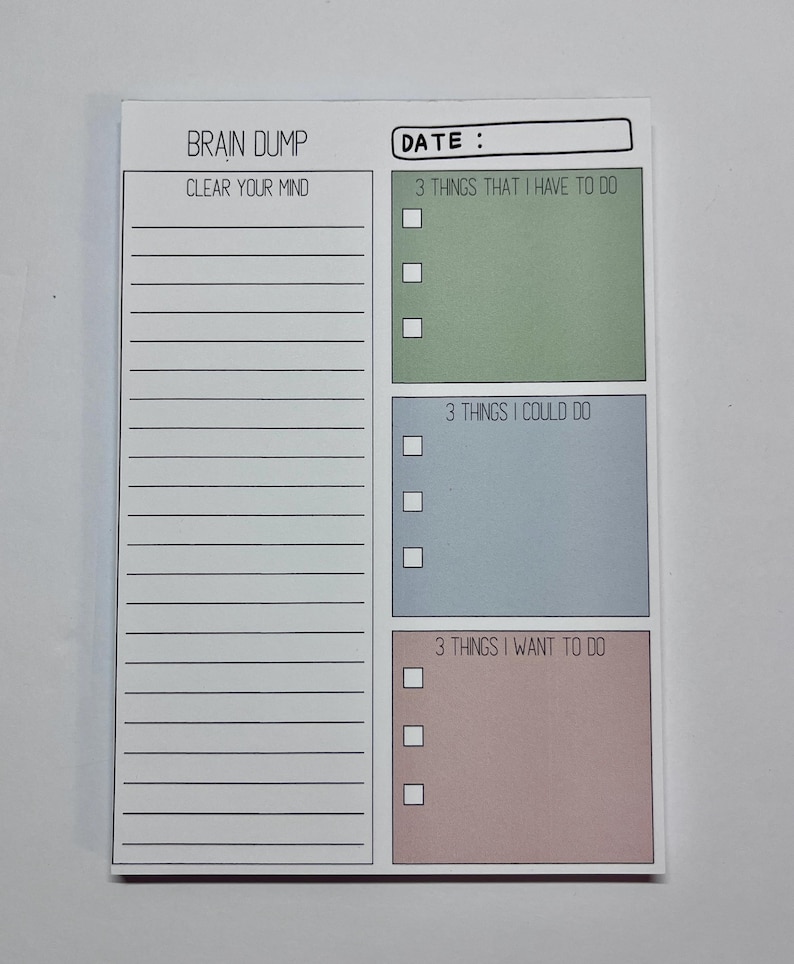 May include: A rectangular paper notepad with a white background featuring a Brain Dump section with horizontal lines. The right side includes three colored boxes labeled 3 Things That I Have To Do in green, 3 Things I Could Do in blue, and 3 Things I Want To Do in pink, each with three checkboxes.