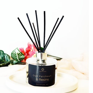 May include: A clear glass bottle with a silver cap and black reeds. The bottle contains a reed diffuser with the label "Oud Patchouli & Resins Reed Diffuser - 6oz".