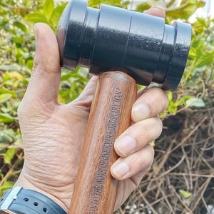 Pode incluir: Um martelo de madeira com uma cabeça de borracha preta. O cabo é gravado com o texto "ONE HEART AT A TIME, THE LOVE OF GOD IS EXTRAORDINARY MAN".