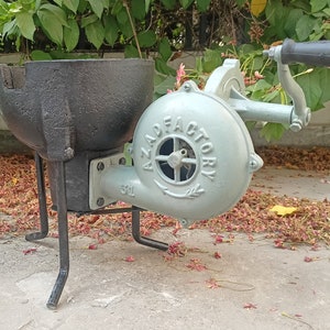 May include: A black cast iron forge with a hand-crank bellows. The bellows is painted light blue and has the text "AZAD FACTORY" on it. The forge is on a set of three black metal legs.