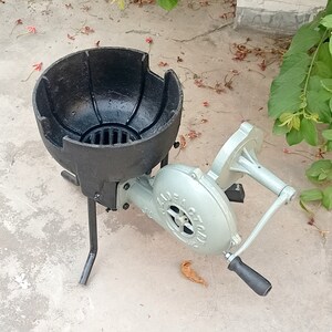 May include: A black cast iron forge with a blower attached. The blower is silver and has a handle. The forge is on a concrete surface.
