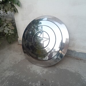 May include: A large, shiny, silver-colored shield with a central star design. The shield has concentric circular patterns and a prominent star emblem in the center. The shield is likely made of metal and has a reflective surface.