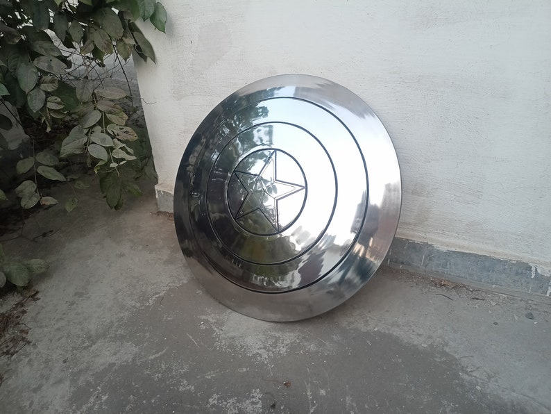May include: A large, shiny, silver-colored shield with a central star design. The shield has concentric circular patterns and a prominent star emblem in the center. The shield is likely made of metal and has a reflective surface.