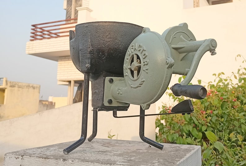 May include: A black cast iron forge with a hand-crank blower. The blower is painted green and has the word "VICTORY" on it. The forge is sitting on a concrete surface.