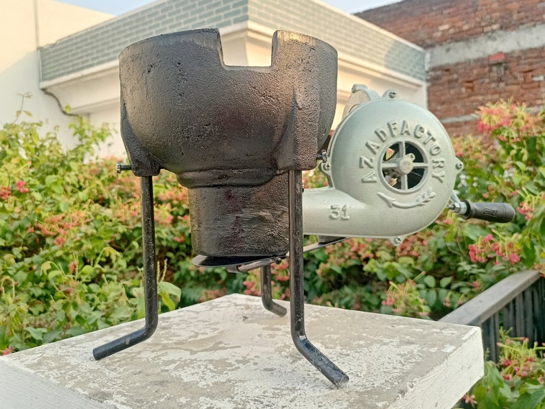 May include: A black cast iron forge with a blower attached. The blower is green and has the text "AZAD FACTORY 51" on it.