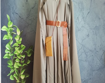 Könnte beinhalten: Ein grauer Kapuzenmantel mit langem, fließendem Design. Der Umhang hat einen geschnürten Ausschnitt, einen braunen Ledergürtel und eine kleine Umhängetasche. Das Outfit wird auf einer Schaufensterpuppe präsentiert.