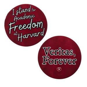 Op de afbeelding: Twee ronde rode knoppen met witte tekst. De eerste knop zegt "Ik sta voor academische vrijheid aan Harvard". De tweede knop zegt "Veritas, Forever" met een klein Harvard-wapen.