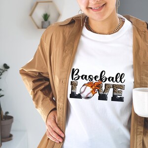 May include: White t-shirt featuring a graphic design of a baseball with flames and the words "Baseball Love" in black and white with a leopard print background.