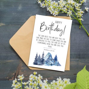 May include: A birthday greeting card with the words "Happy Birthday!" in elegant script. The card features a watercolor illustration of mountains and trees in shades of blue and gray, with a Bible verse below.
