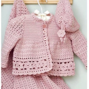 Peut inclure: Un ensemble de vêtements pour bébé en crochet rose comprenant un cardigan, une jupe et un chapeau. Le cardigan est doté d'une fermeture à bouton et d'une délicate bordure en crochet. La jupe est trapèze et le chapeau est orné d'une fleur.