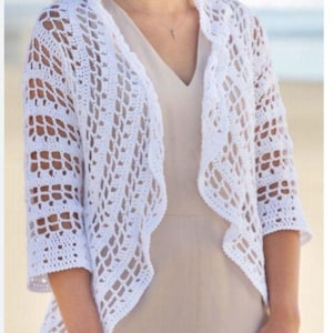 May include: A white, open-weave crochet jacket with three-quarter sleeves. The jacket has a scalloped edge and is worn over a neutral-coloured outfit. The crochet pattern creates an airy, textured look, suitable for layering.