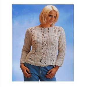 May include: A crocheted top with a delicate openwork design. The top is cream coloured and has long sleeves. The model is wearing blue jeans.