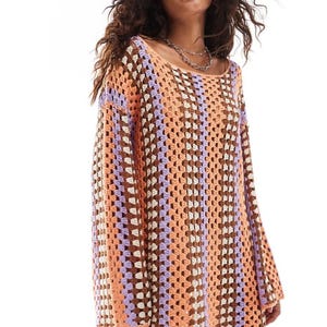 May include: A multi-coloured crochet dress with a loose, open weave. The dress has vertical stripes in peach, brown, lavender, and white. It features long sleeves and a scoop neckline, suitable for casual wear.