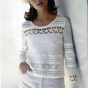 Könnte beinhalten: Ein weißes Häkeltop mit einem zarten Lochmuster. Das Top hat lange Ärmel und einen runden Ausschnitt.