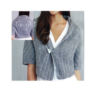 May include: A gray crocheted shrug with short sleeves and a shawl collar. The shrug is open in the front and has a silver clasp.