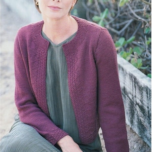 Puede incluir: Una mujer lleva un cárdigan morado con cuello redondo y mangas largas. El cárdigan está hecho de lana merino aran y tiene una talla de 32-42 pulgadas.