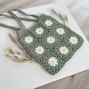 May include: A green crocheted tote bag with white daisy flowers. The bag has two straps and is made with a granny square stitch.