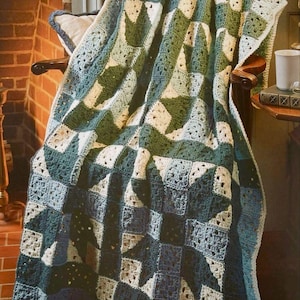 May include: A crocheted throw blanket with a patchwork design in shades of green, blue, and white. The blanket is draped over a chair in front of a fireplace.