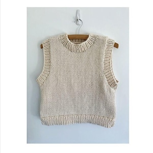 May include: A cream-coloured sleeveless knitted vest with a round neckline. The vest is hanging on a wooden hanger.