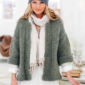 May include: A green knitted cardigan with a white scarf and a gray beanie. The cardigan has a simple design and is made of a soft, textured yarn.