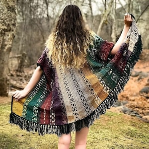 May include: A colorful crochet poncho with fringe trim. The poncho is made with a variety of colors, including green, red, purple, and yellow. The poncho is worn by a person with long, curly hair.