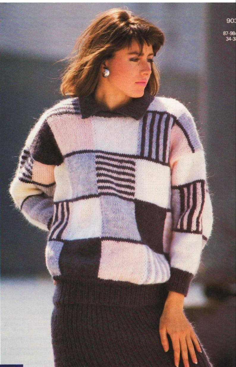 Pu&ograve; includere: Un maglione patchwork nei toni del bianco, rosa, grigio e marrone scuro. Il maglione ha un collo e polsini e orlo a coste. La persona indossa anche una gonna marrone scuro abbinata.