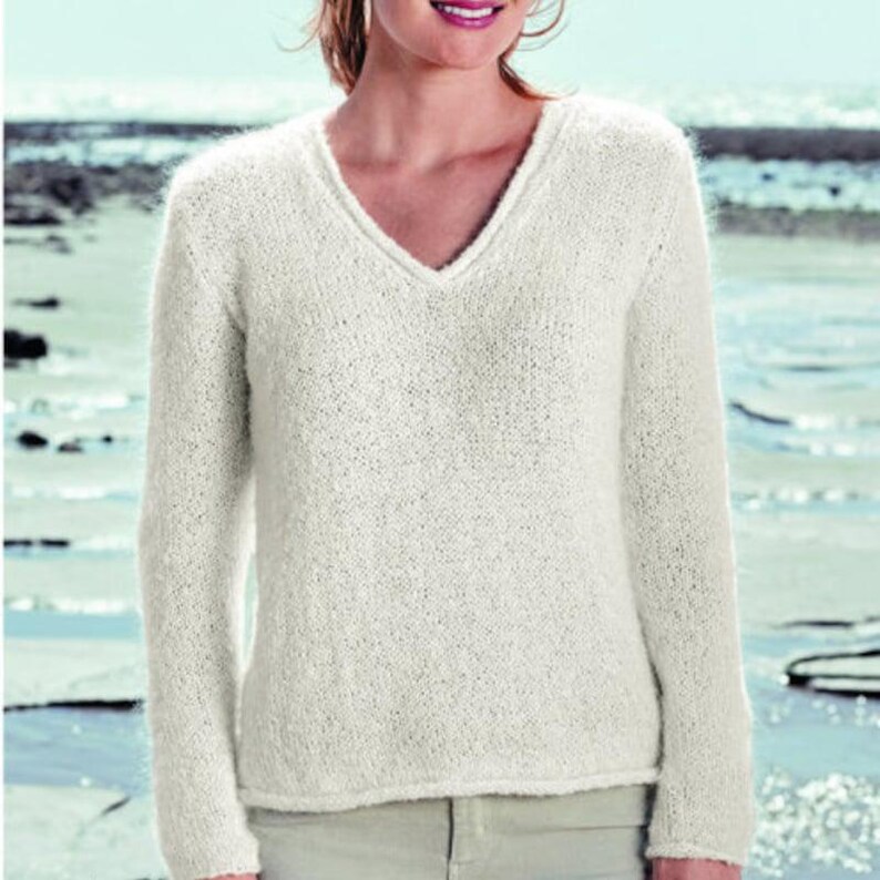 May include: A white knitted sweater with a v-neck and long sleeves. The sweater is made of a soft, fluffy yarn.