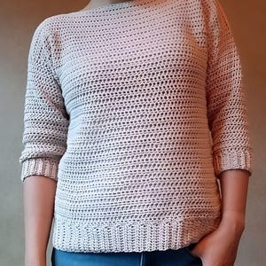 May include: A light beige crocheted sweater with a loose fit and three-quarter sleeves.