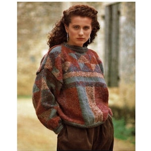 Könnte beinhalten: Eine Frau trägt einen braunen, blauen und roten gemusterten Pullover mit Rundhalsausschnitt. Sie steht vor einer Steinmauer.