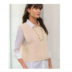 Può includere: Un gilet di uncinetto color crema con una trama larga e aperta. Il gilet è senza maniche e ha una scollatura rotonda. La modella indossa il gilet sopra una camicia bianca abbottonata.